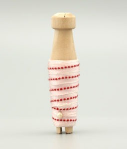 Tetilband i vitt med röd detalj trädd på en träspole